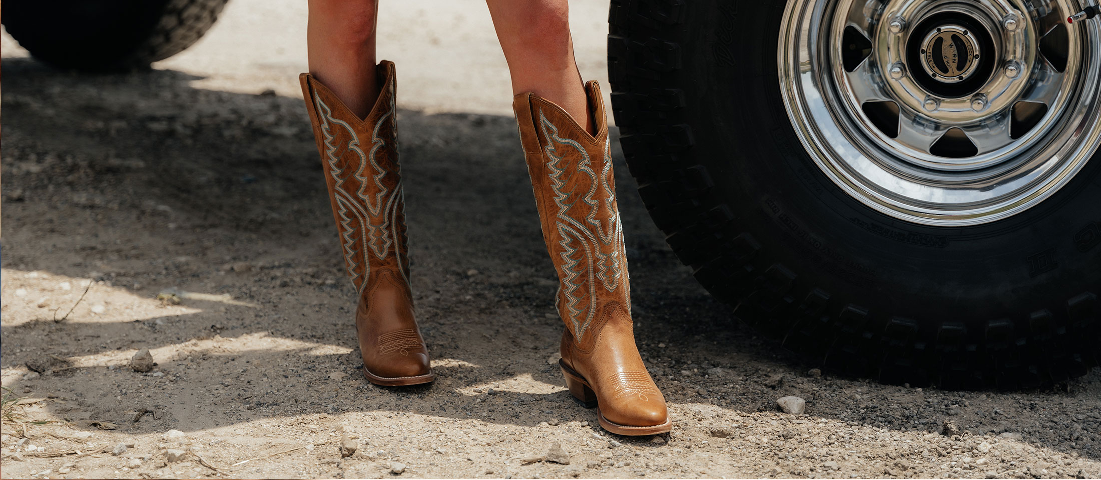 A woman wearing Justin western boots while standing next to a truck.